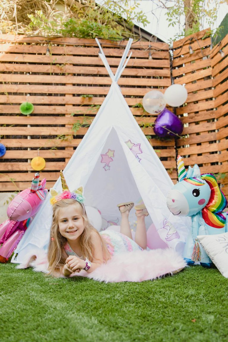 A young girl having fun at a unicorn-themed outdoor birthday party with vibrant decorations.
